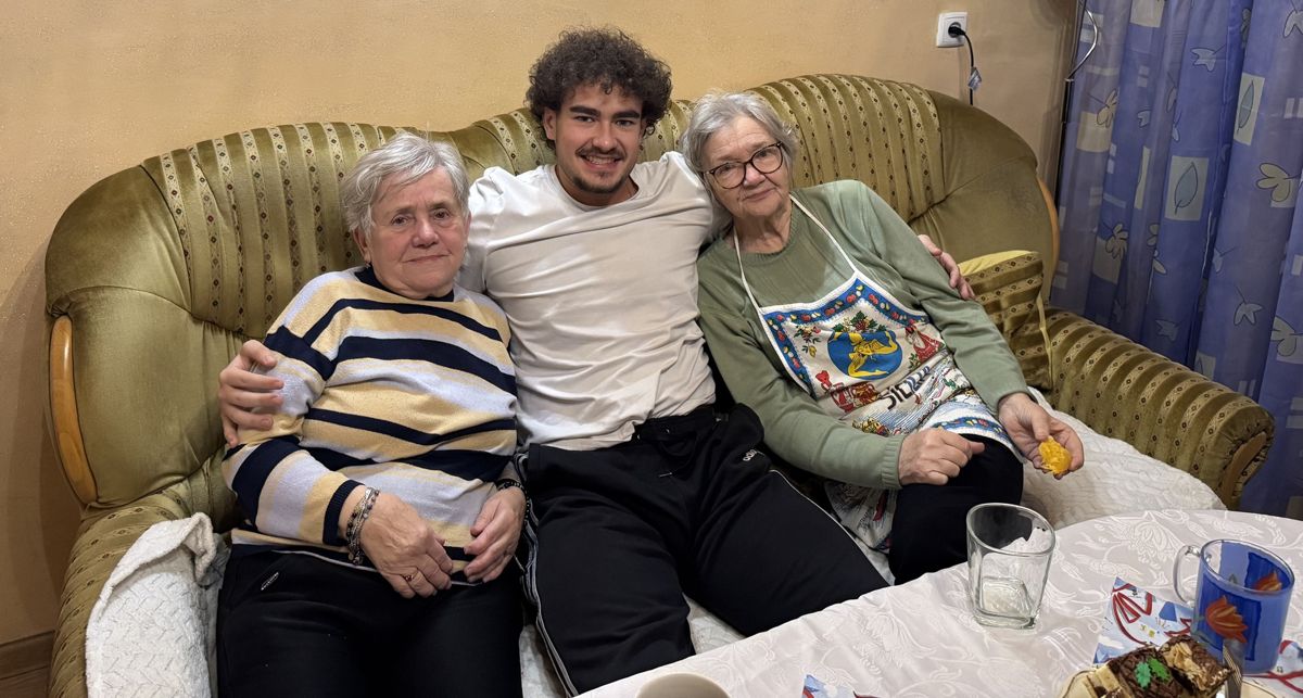 Fabian mit zwei älteren Damen auf einem Sofa, davor ein Tisch mit Tee und Kuchen
